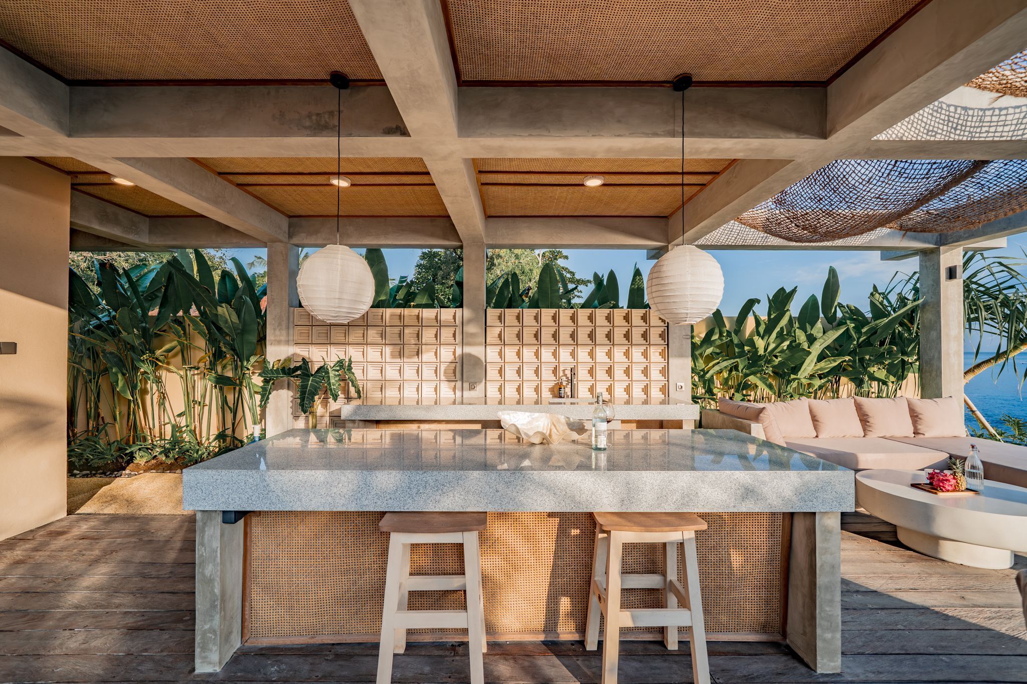 A modern outdoor kitchen with a central island, bar stools, and a seating area with a view of the ocean.