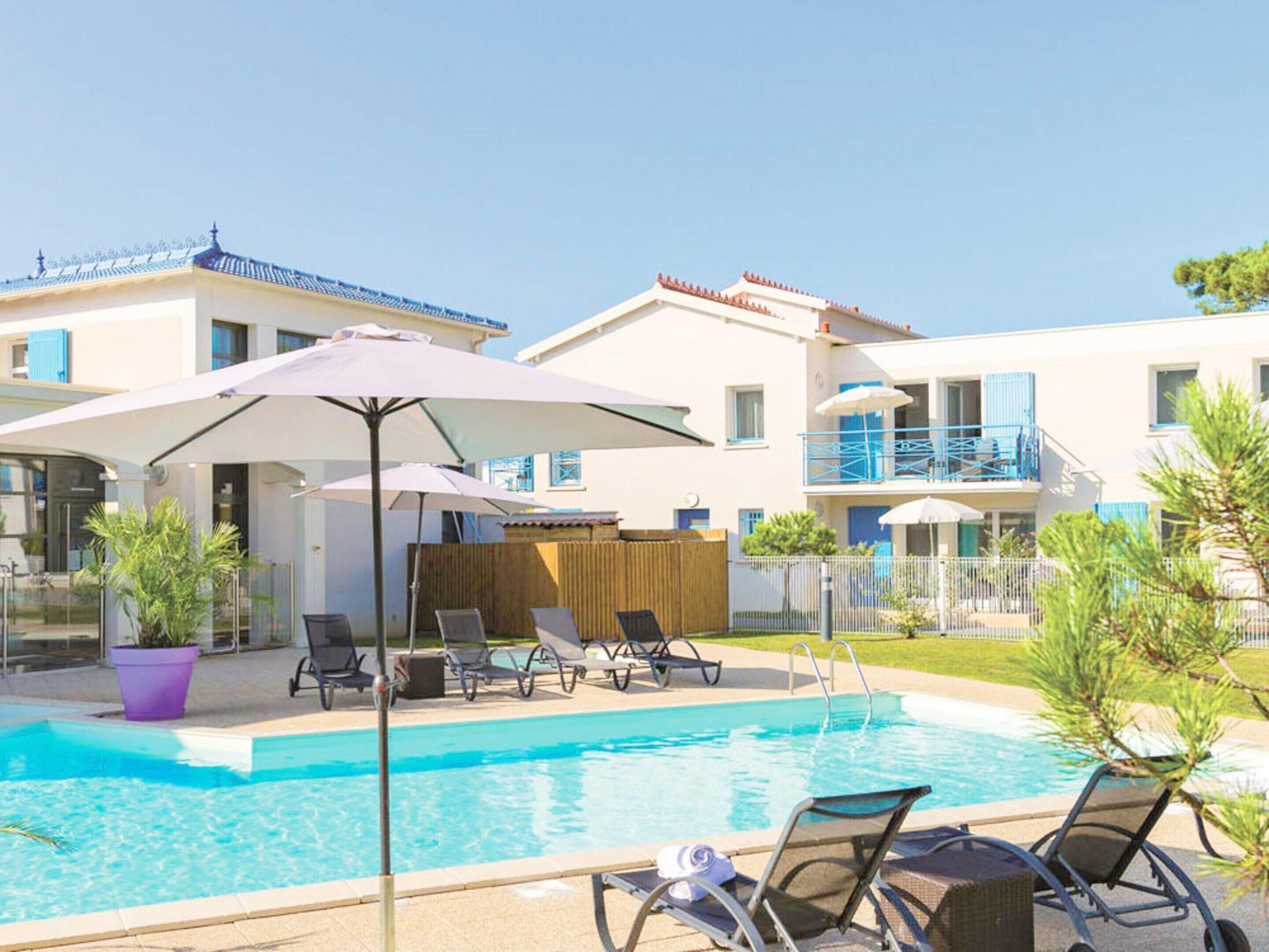 Une piscine entourée de bâtiments dotés de balcons, avec des chaises longues et des parasols à proximité.