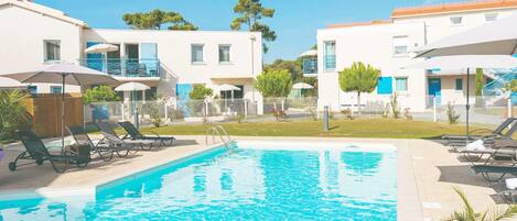 A swimming pool with lounge chairs, a fenced area, and buildings with balconies and windows.