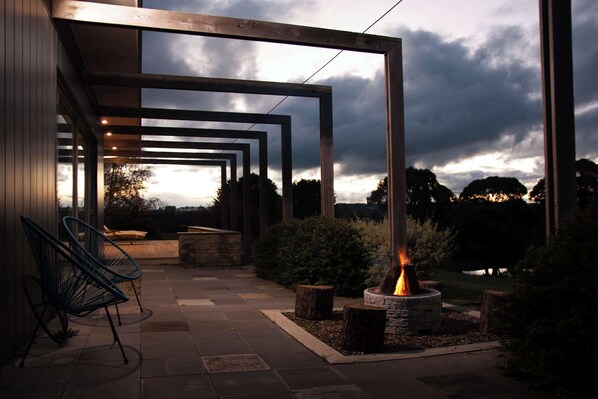 An outdoor patio with a fire feature, chairs, and a stone planter.