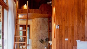 A bedroom with a curved wooden bed, a stone wall, and a wooden ladder. - Malai Khaoyai (Pak Chong)