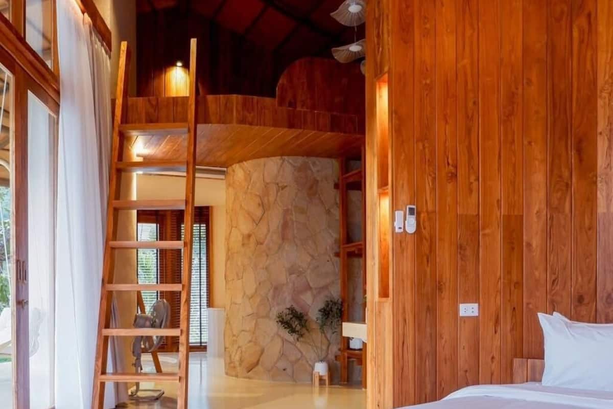 A bedroom with a curved wooden bed, a stone wall, and a wooden ladder.