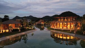 A serene lakeside hotel with a reflective pool, wooden structures, and a view of distant hills. - Malai Khaoyai (Pak Chong)
