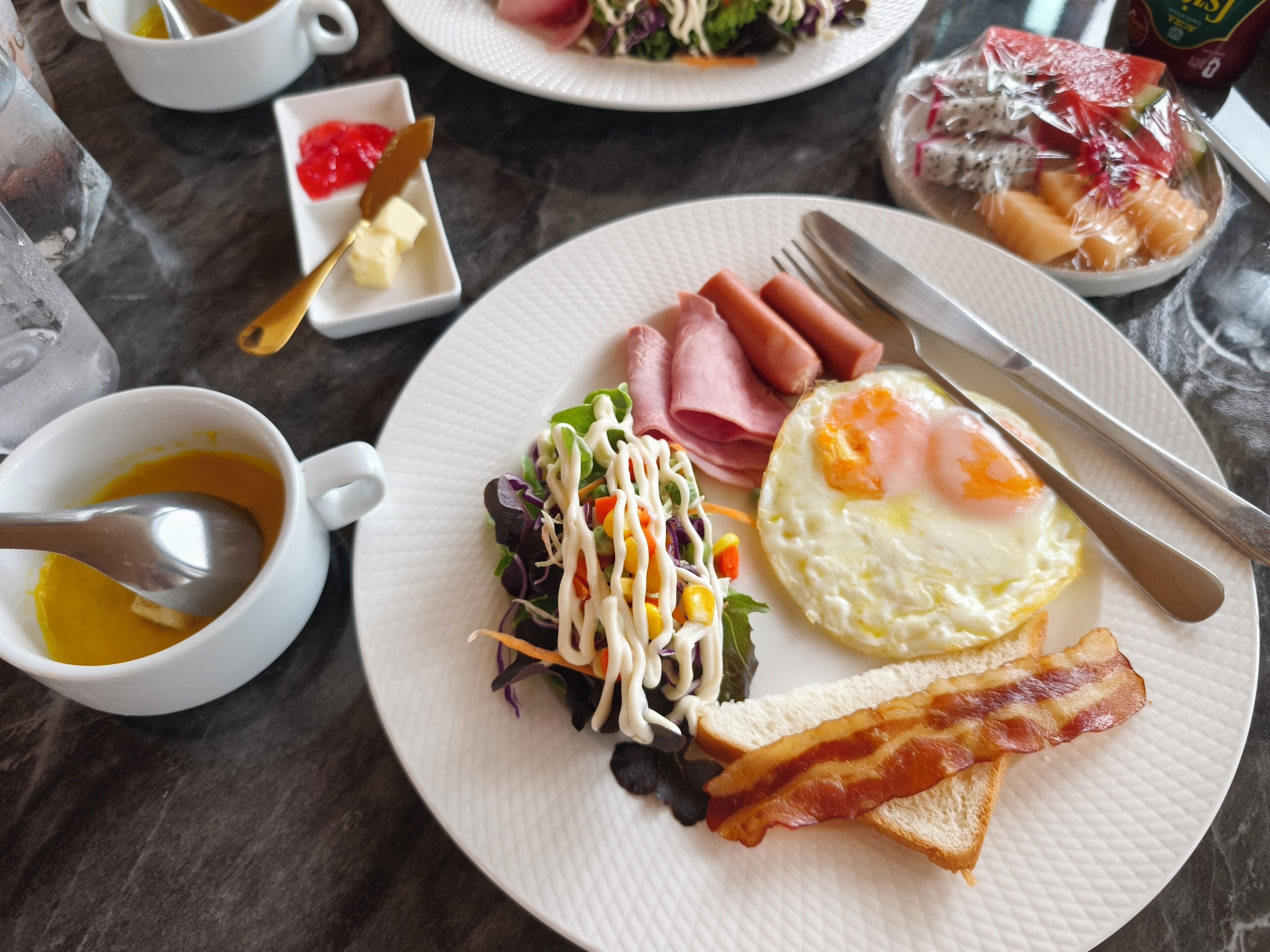 A breakfast plate with eggs, bacon, ham, and a salad.