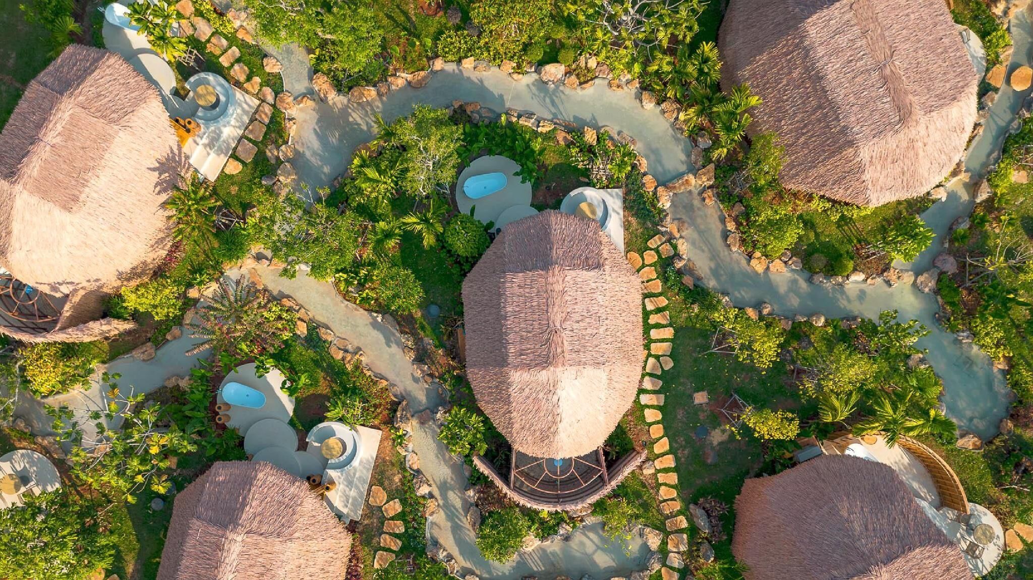 A resort with multiple thatched-roof structures, interconnected pathways, and a central water feature.