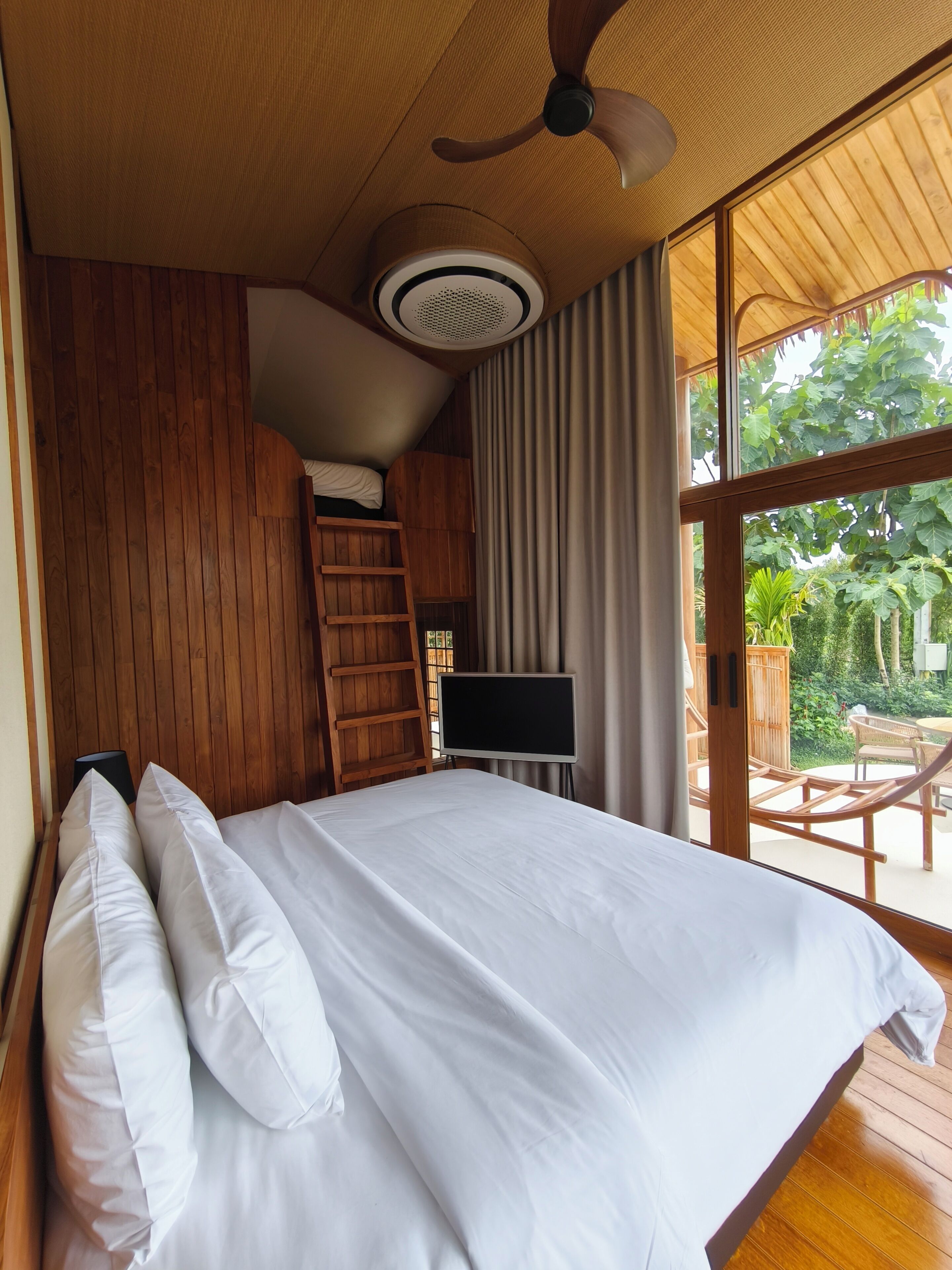 A bedroom with a bed, a desk, a ladder, and a ceiling fan.