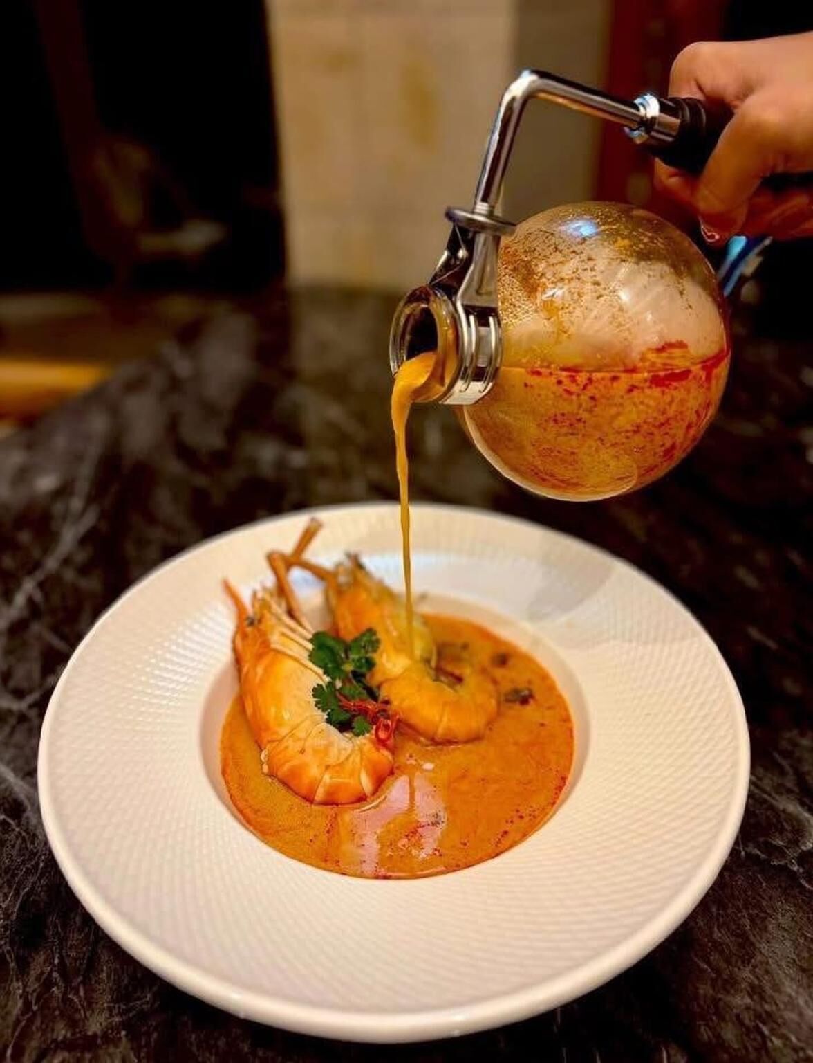 Un plato con camarones y salsa vertiéndose de una jarra de metal.