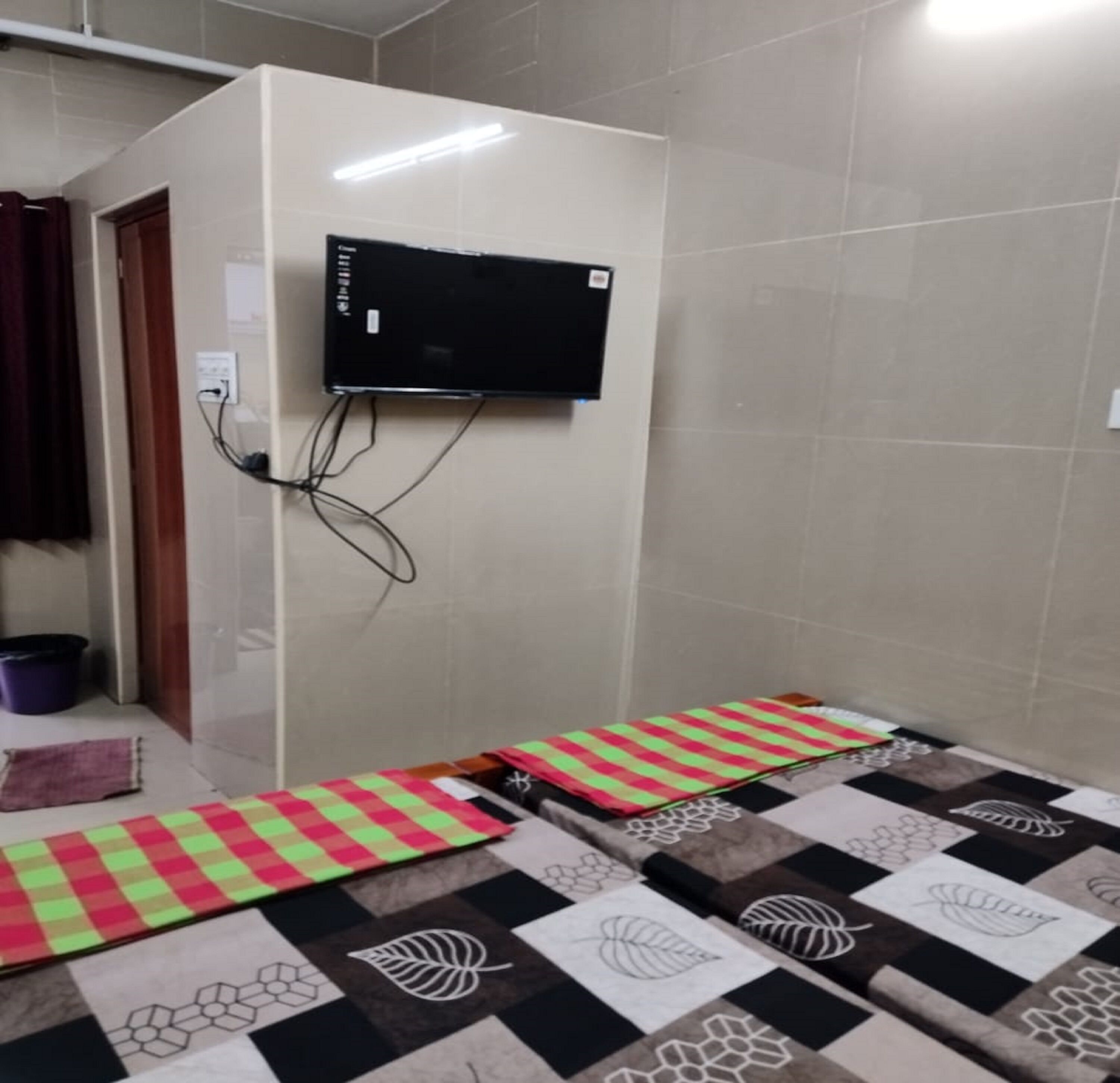 A room with a flat-screen TV mounted on the wall, a patterned rug, and a door leading to another room.