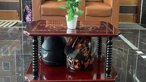 A lobby with a brown leather sofa, a red table with a white vase, and a helmet on the table. - Mahilagam (Chennai)