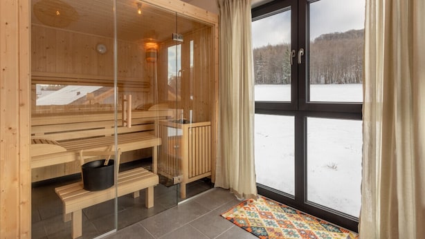 Una sauna con panche in legno, una parete divisoria in vetro e vista su un paesaggio innevato attraverso ampie finestre.