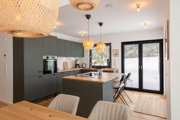 A modern kitchen with grey cabinets, a wooden island, and pendant lighting.
