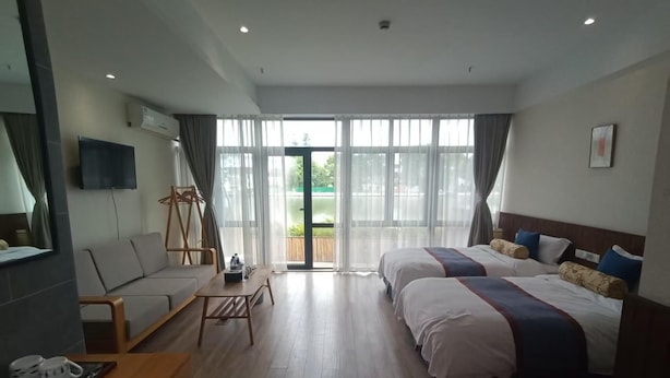 Habitación de hotel con dos camas, un sofá, una mesita pequeña y un ventanal grande.