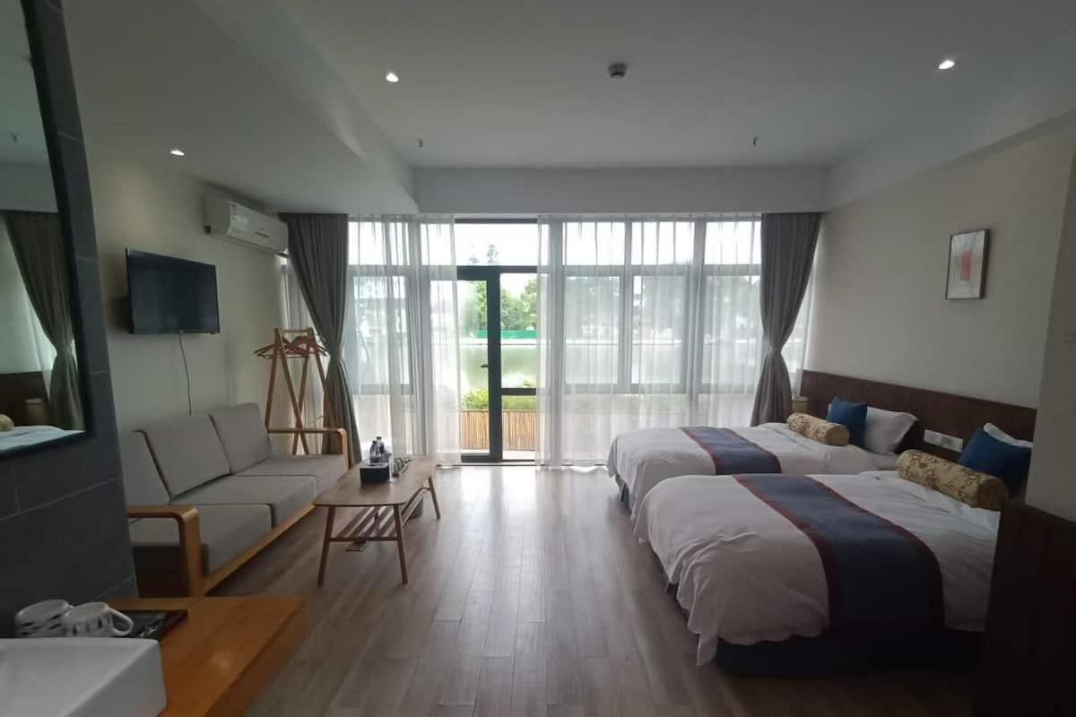 A hotel room with two beds, a sofa, a small table, and a large window.