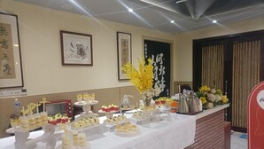 Una mesa de buffet con diferentes alimentos, obras de arte en las paredes y un mostrador de recepción con un letrero rojo.