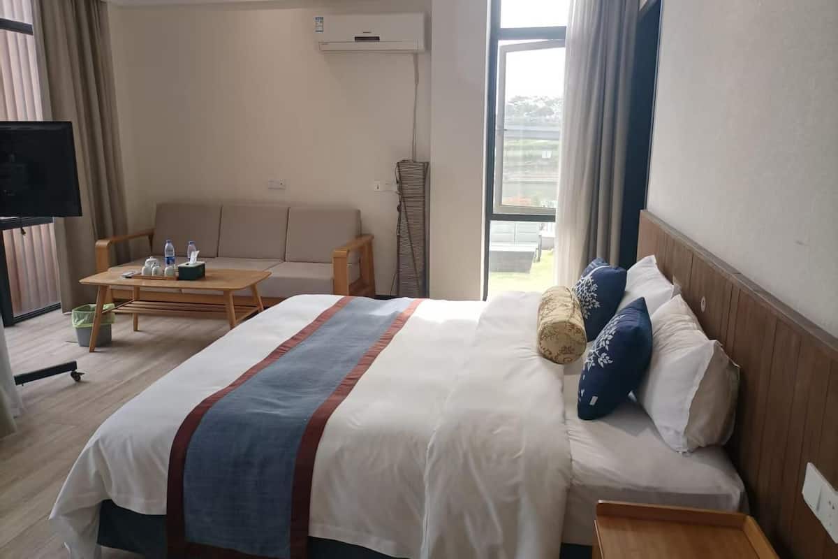 A hotel room with a bed, a sofa, a small table, a TV, and a balcony.