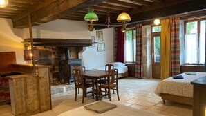 Une pièce rustique avec une cheminée en pierre, des meubles en bois et un lit recouvert d’une courtepointe blanche.