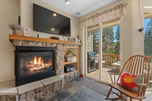 Ein Kamin mit Steinverkleidung, darüber ein Flachbildfernseher und eine Holzterrasse mit Gartenmöbeln.