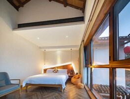 Ein Schlafzimmer mit Bett, Sessel, Sitzsack, Nachttisch und einem großen Fenster.