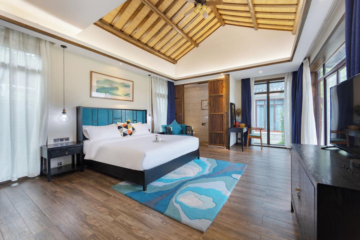 Un dormitorio moderno con una cama grande, suelo de madera, ventilador de techo y televisión.
