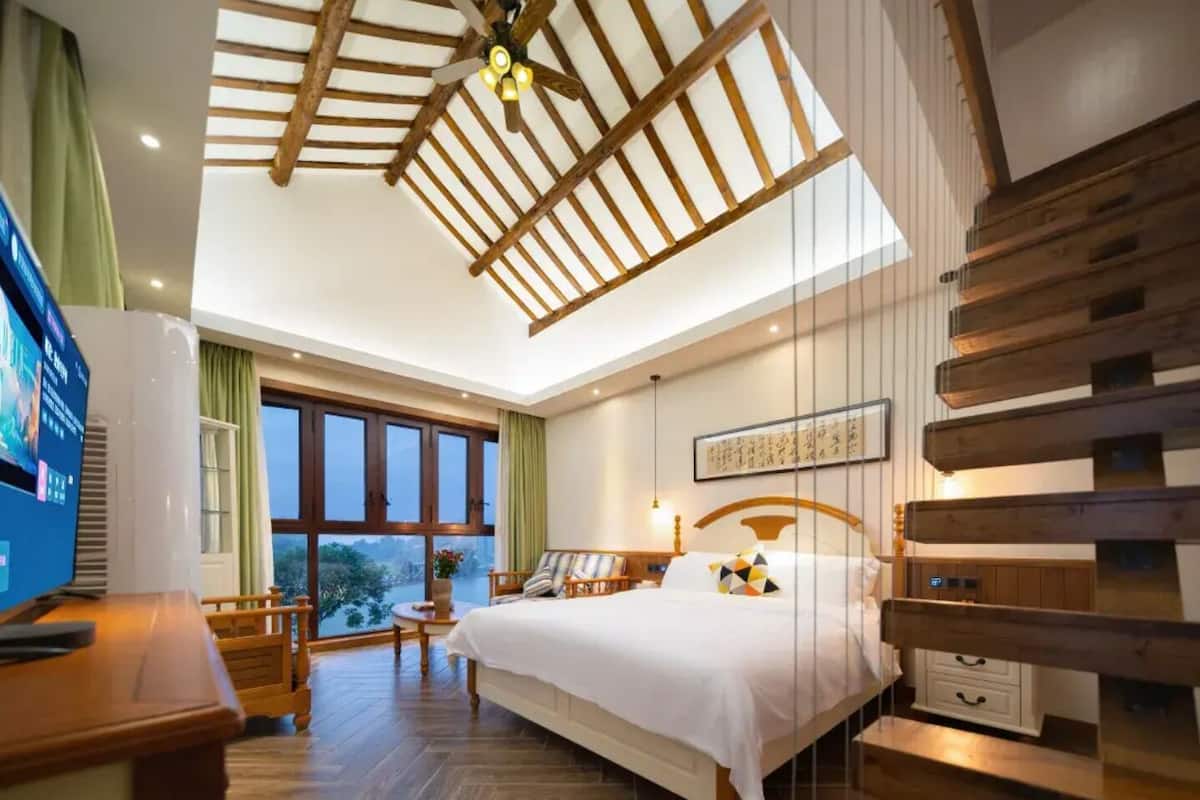 Un dormitorio con cama, vigas de madera en el techo, una ventana y vistas a zonas verdes.