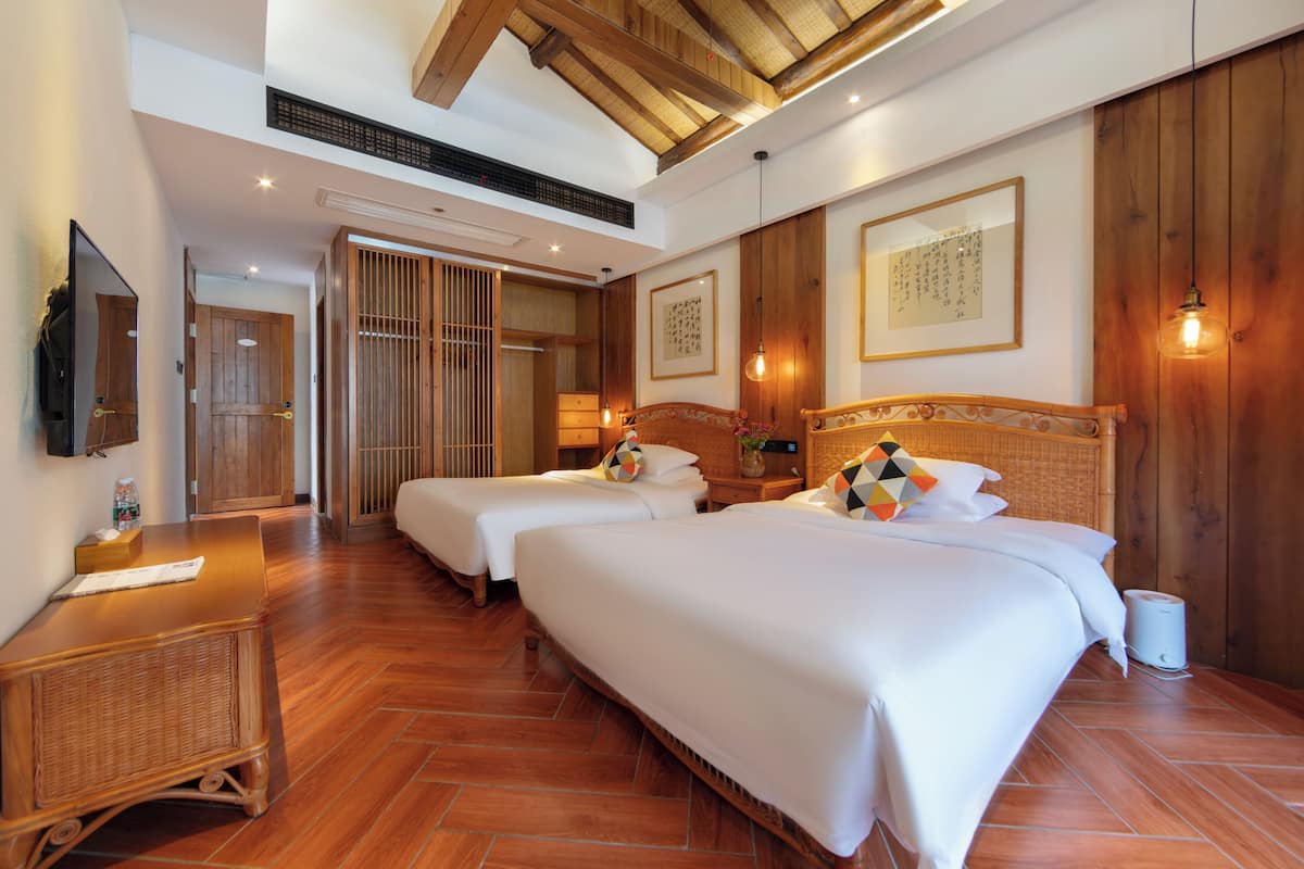 Habitación de hotel con dos camas, suelo de madera, ventilador de techo, televisor montado en la pared y puerta corredera de estilo japonés tradicional.