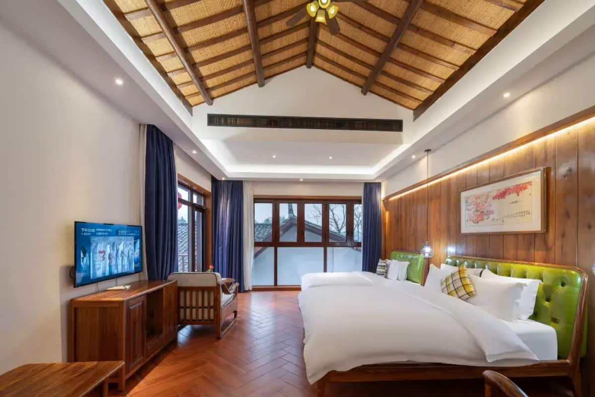 Habitación de hotel con techo de madera, cama con tapicería verde, televisor en la pared y un ventanal grande.
