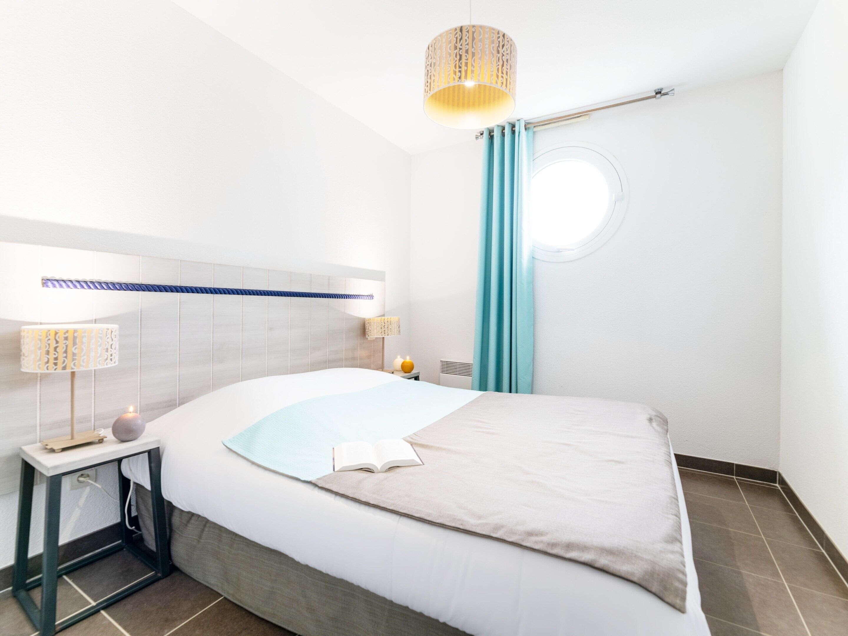 Een moderne hotelkamer met een groot bed, bedlampjes, een klein tafeltje en een raam met gordijnen.