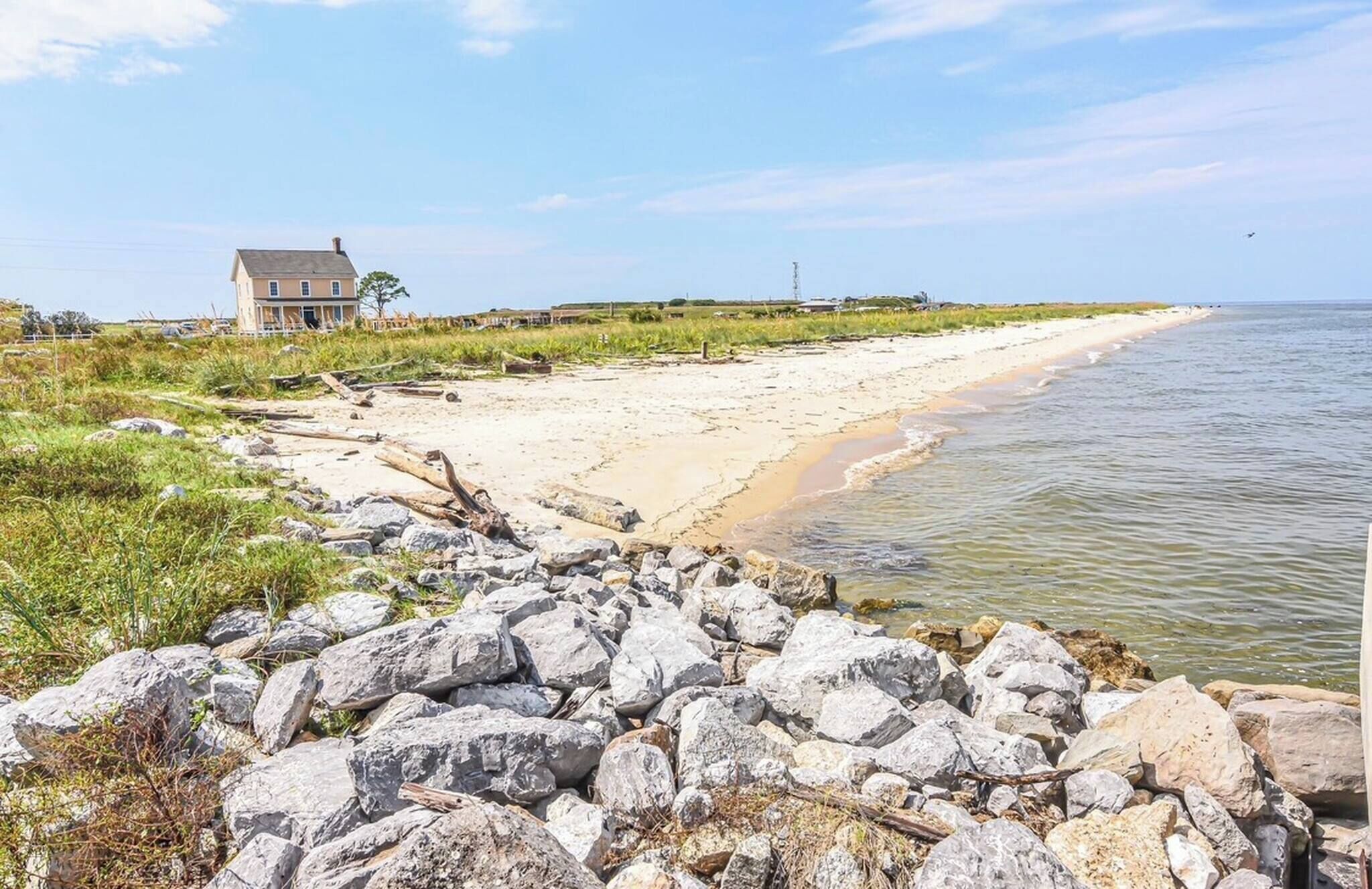 Uma propriedade costeira com uma praia de areia, primeiro plano rochoso e uma casa com varanda grande.