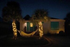 Ein Haus mit zwei Palmen, die mit Lichterketten umwickelt sind, einer Hängematte und einem Sternenhimmel.