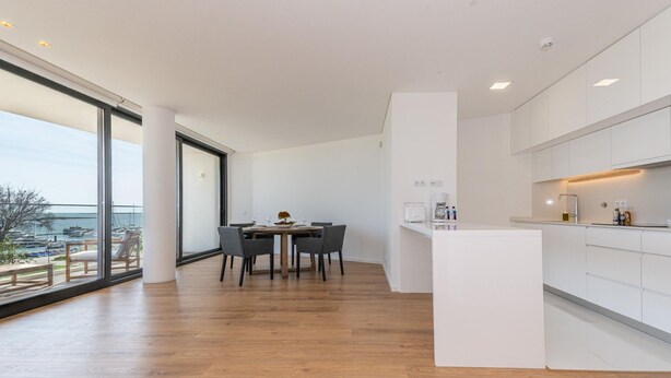 Una cocina moderna con una isla central, ventanas amplias y una zona de comedor con mesa y sillas.