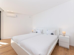 A modern, minimalist bedroom with two single beds, white bedding, bedside tables with lamps, and a wooden floor. - OL Retreat 4 2 AE in Olh o (Olhao)