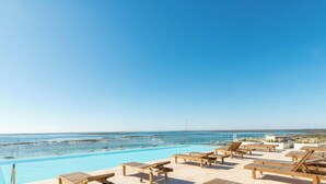 Un área junto a la piscina con sillones de descanso y una vista despejada del océano.
