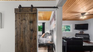 A room with a bed, a desk, a TV, and a sliding barn door. - Bear Ridge BaseCamp at Buffalo Creek | Pet-Friendly Lake Lure Cabin with Views, Firepit & Game Room (Lake Lure)