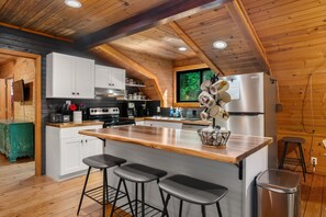 Een moderne keuken met houten balken, een groot kookeiland met barstoelen, witte kasten en een roestvrijstalen koelkast.