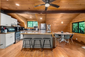 Een moderne keuken met houten wanden, een centraal kookeiland met barkrukken, een koelkast, en een eethoek met een tafel en stoelen.