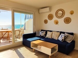 Ein Wohnzimmer mit Sofa, Couchtisch und Meerblick durch eine Schiebetür.