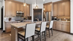 Une cuisine moderne avec des meubles en bois, des appareils électroménagers en acier inoxydable et un îlot central doté de tabourets de bar.