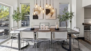 Un espace repas avec une table dressée pour six personnes, entourée de chaises, et des lampes suspendues au-dessus.