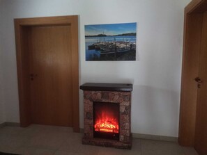 A room with a fireplace, a door, and a painting of a lakeside scene.