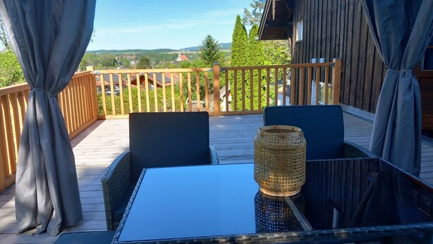 Una terraza de madera con una mesa y sillas, una cesta de mimbre y vistas a un pueblo.
