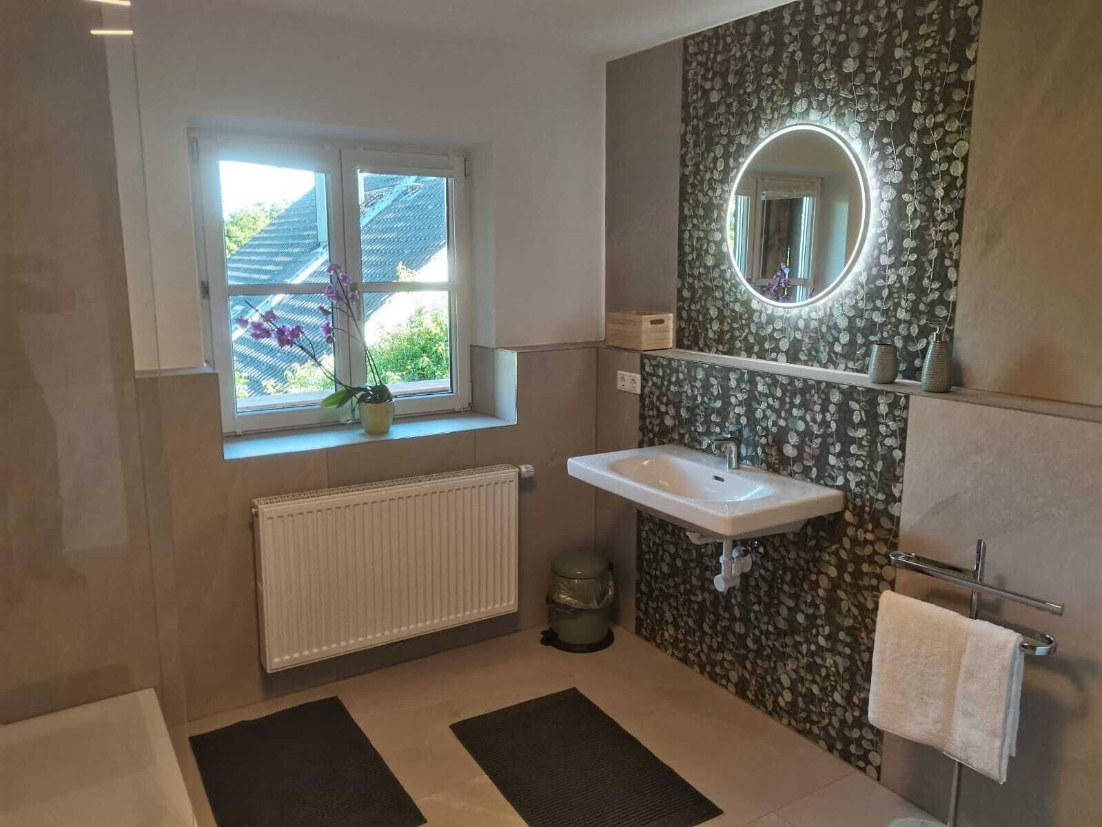 Une salle de bain avec une fenêtre, un lavabo, un miroir, un radiateur et un porte-serviettes.