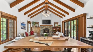 A spacious living area with a large wooden table, a stone fireplace, and a high ceiling with exposed beams. - Luxury Tamarack Cottage | Ski-In/Ski-Out | Hot Tub | Walk to Village (Donnelly)