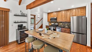 A modern kitchen with wooden cabinets, stainless steel appliances, a wooden island with stools, and a staircase leading to another level. - Luxury Tamarack Cottage | Ski-In/Ski-Out | Hot Tub | Walk to Village (Donnelly)