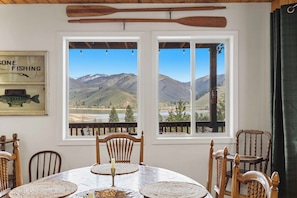 A dining area with a table, chairs, and a view of mountains through large windows.