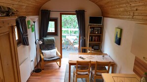 A cozy room with a wooden ceiling, a small table with chairs, a bookshelf, and a window with curtains.