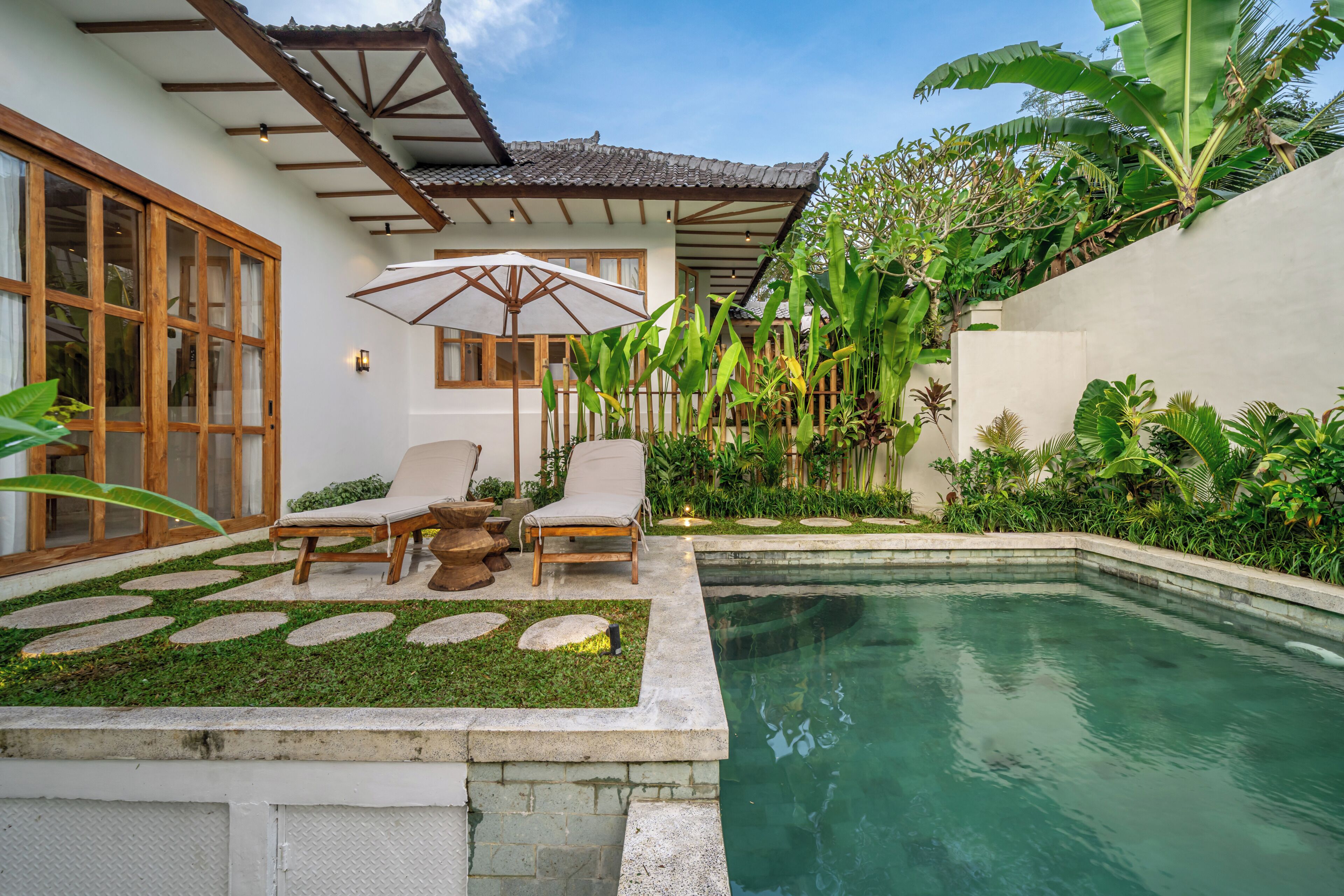 A pool area with lounge chairs, a pergola, and tropical plants.