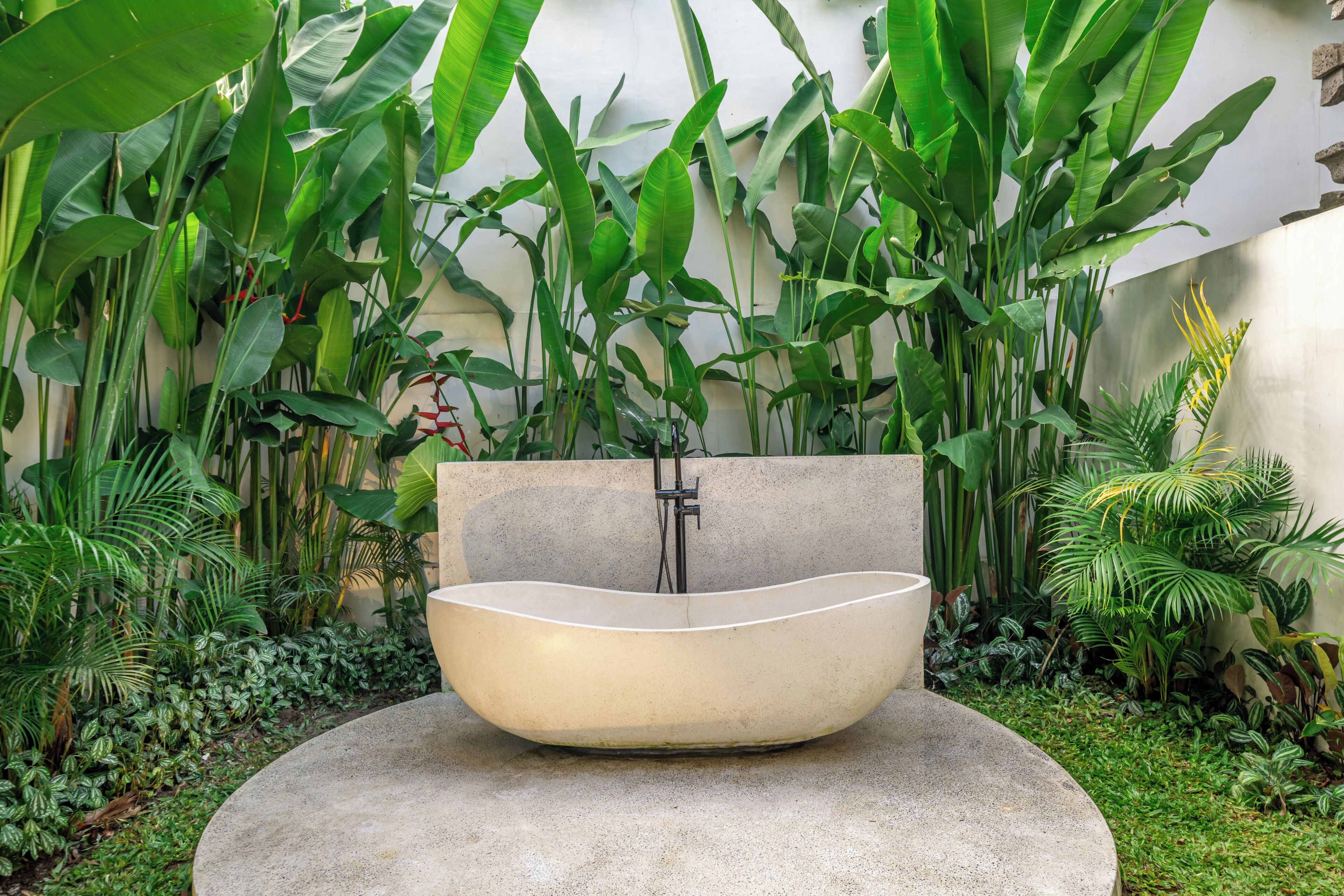 Un baño exterior moderno con un lavamanos grande y curvo, rodeado de exuberante follaje tropical.