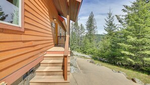 En träbyggnad med en veranda, trappsteg som leder upp till en dörr och utsikt över ett skogsområde.