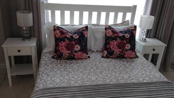 A bed with floral pillows, a white headboard, and bedside lamps on white nightstands.