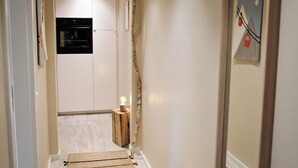 Un couloir étroit doté d’un plancher en bois, une petite table avec une lampe et une porte surmontée d’un appareil noir.